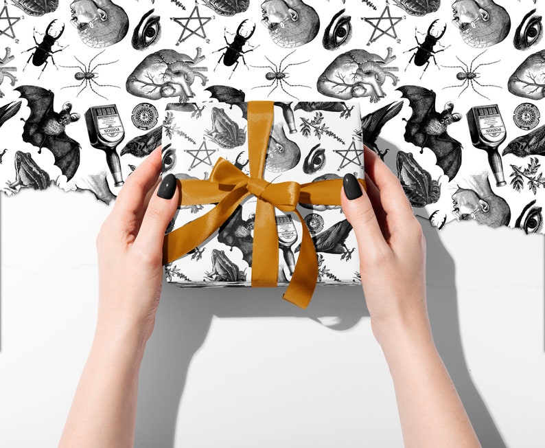 Monochrome witch craft artwork on wrapping paper, a box being held in two hands with an orange ribbon