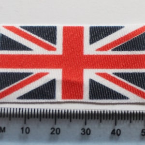 May include: A small, printed fabric patch featuring the Union Jack flag of the United Kingdom. The flag is red, white, and blue with a textured fabric design.
