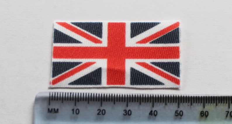May include: A small, printed fabric patch featuring the Union Jack flag of the United Kingdom. The flag is red, white, and blue with a textured fabric design.