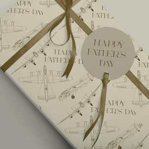 May include: Gift-wrapped present with a beige background. The wrapping paper features a repeating pattern of airplane illustrations. A beige ribbon and a circular tag that reads "HAPPY FATHER'S DAY" complete the gift.