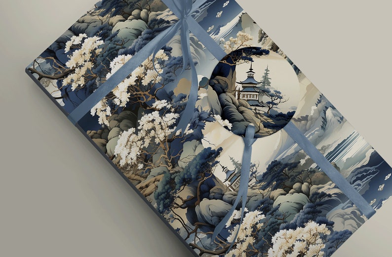 May include: A rectangular gift box wrapped in paper featuring a dark blue and cream landscape illustration of mountains, trees, and a pagoda. A blue ribbon is tied around the box, securing a circular gift tag with a matching pagoda scene.
