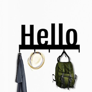 Puede incluir: Perchero de pared de metal negro con la palabra "Hello" en letras grandes. El perchero tiene tres ganchos con un sombrero, una mochila y una camisa colgados.