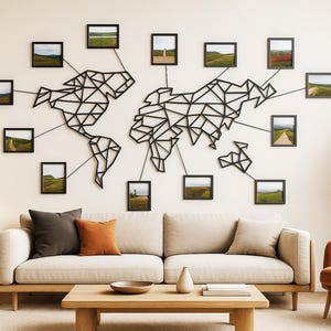 Peut inclure: Un salon moderne présente une décoration murale en forme de carte du monde en métal noir avec de petites photos de paysages encadrées. Un canapé beige avec des coussins, une table basse en bois et un fauteuil orange complètent le décor.