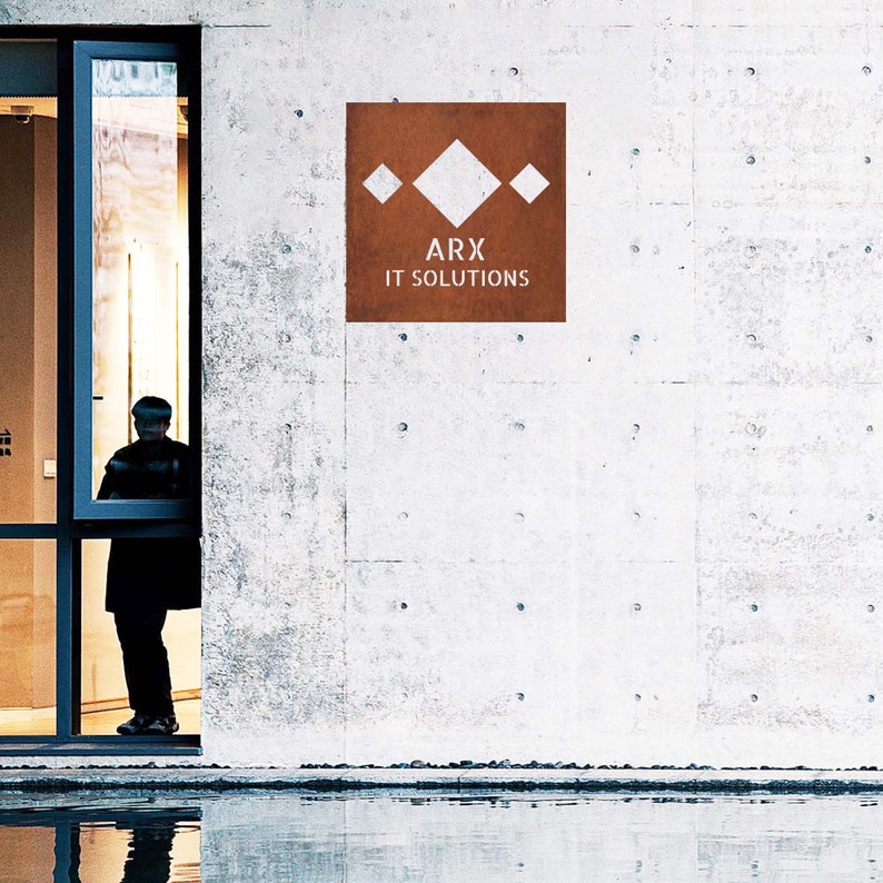 May include: A brown rectangular sign with a white geometric design and the text "ARX IT SOLUTIONS" on a white concrete wall.