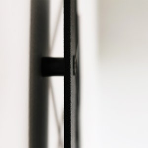 May include: A black metal wall-mounted sign with a rounded corner and a single screw visible.