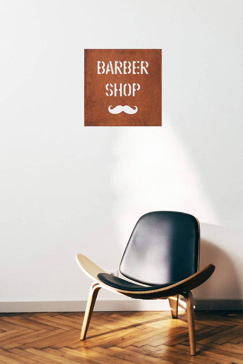 May include: A brown sign with white lettering that reads "BARBER SHOP" and a white moustache underneath. A black leather chair with wooden legs sits on a wooden floor.