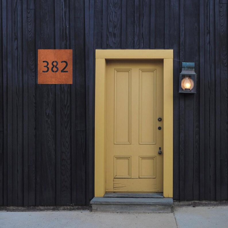 May include: A yellow door with a black wooden frame and a black metal light fixture on the side. The door has a number "382" on the wall above it.