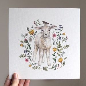 May include: A watercolor painting of a white lamb with a small bird perched on its head. The lamb is surrounded by a wreath of colorful flowers, including yellow, pink, and purple.