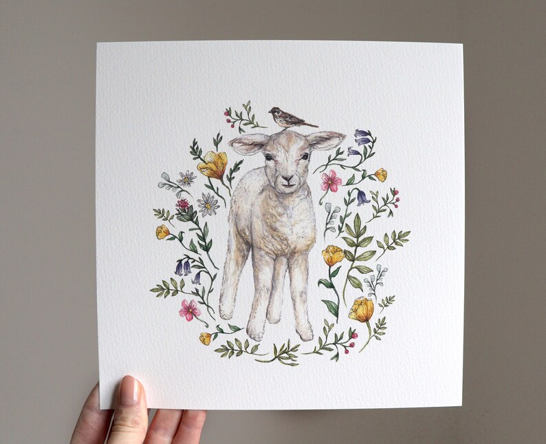 May include: A watercolor painting of a white lamb with a small bird perched on its head. The lamb is surrounded by a wreath of colorful flowers, including yellow, pink, and purple.