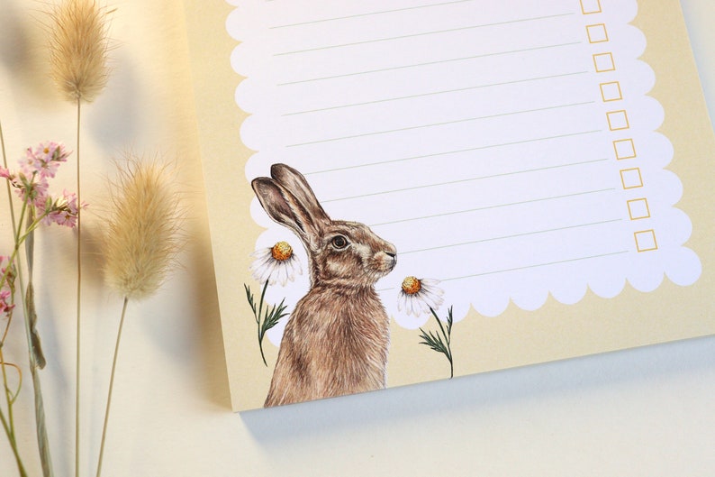 May include: A cream-colored notepad with a scalloped edge and a checklist. The notepad features a brown hare illustration with white daisies.