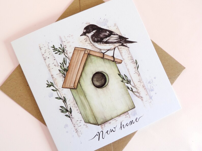 May include: A watercolor illustration of a bird perched on a green birdhouse with a brown roof. The birdhouse is surrounded by birch trees and green leaves. The text "New home" is written in cursive at the bottom of the card.