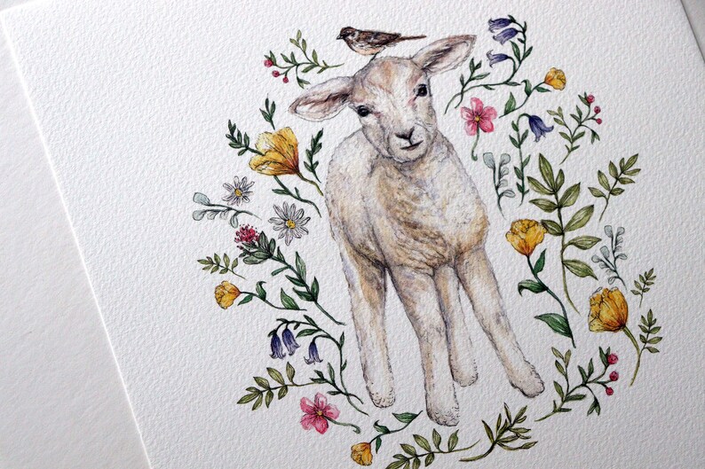 May include: A watercolor painting of a white lamb with a small bird perched on its head. The lamb is surrounded by a wreath of colorful flowers, including yellow, pink, and purple.