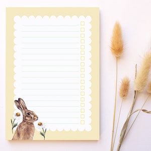 May include: A yellow notepad with a scalloped edge and a brown rabbit illustration. The notepad has lined paper and a checklist with empty boxes.