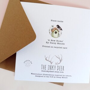 May include: A white card with a brown envelope. The card has a watercolor illustration of a birdhouse with a bird on top. The text on the card reads "Blank inside", "'A New Home' By Daisy Maude", "Printed on recycled card", "THE INKY DEER", "theinkydeer.etsy.com", "Watercolour illustrations inspired by nature, designed in the U.K by Daisy Maude".