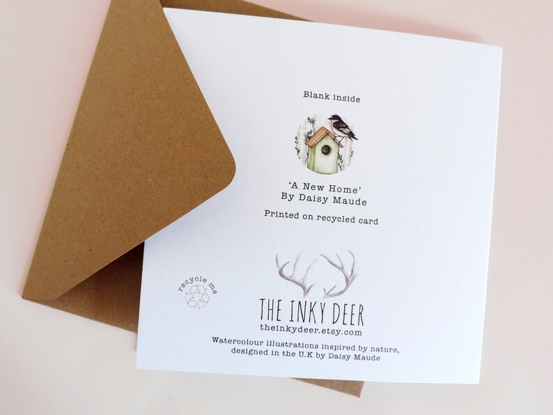 May include: A white card with a brown envelope. The card has a watercolor illustration of a birdhouse with a bird on top. The text on the card reads "Blank inside", "'A New Home' By Daisy Maude", "Printed on recycled card", "THE INKY DEER", "theinkydeer.etsy.com", "Watercolour illustrations inspired by nature, designed in the U.K by Daisy Maude".