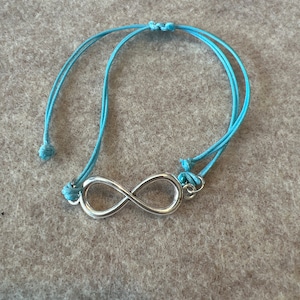 May include: A light blue string bracelet with a silver infinity symbol charm.