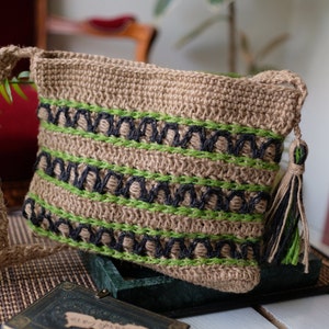 Puede incluir: Un bolso de crochet marrón y verde con un borla negra. El bolso tiene un diseño tejido con rayas negras y verdes.