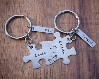 May include: Two silver keychains with puzzle pieces that fit together. One piece says "Laura" and the other says "Caitlin". The keychains also have tags that say "Best Friends".