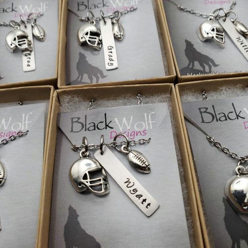 May include: A silver-toned necklace featuring a football helmet charm, a football charm, and a rectangular metal tag engraved with the name Wyatt. The jewelry is presented on a display card labeled Black Wolf Designs with a wolf silhouette.