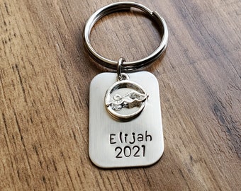 May include: Silver keychain with a swimmer charm and a rectangular tag that says "Elijah 2021".