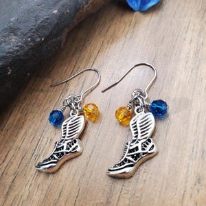 May include: Silver earrings with a winged shoe charm, blue and yellow crystal beads.