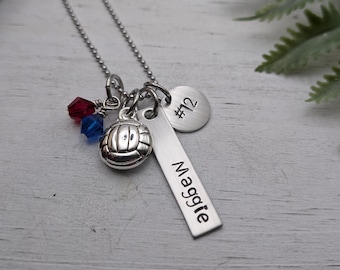 May include: A silver-toned necklace featuring a ball charm, a rectangular bar pendant engraved with the name Maggie, a circular disc pendant engraved with #12, and two small faceted crystal beads in red and blue attached to a ball chain.