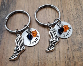 May include: Two silver keychains with a winged shoe charm and a round tag with the names "Gianna" and "Leslie" engraved on them. Each tag has a black and orange crystal.