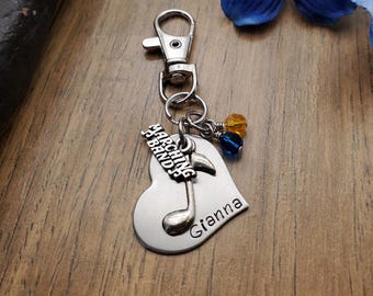 May include: Silver heart-shaped keychain with a musical note charm and the words "Marching Band" and "Gianna" engraved on it. The keychain also has blue and yellow beads.