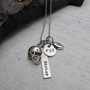 May include: A silver-toned ball chain necklace featuring three charms: a miniature football helmet, a round disc engraved with #33, and a rectangular vertical bar tag engraved with the name Bishop, accompanied by a small football charm.