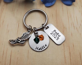 May include: Silver keychain with a winged shoe charm, two small green and orange crystals, and two silver tags. One tag says "Hailie" and the other says "Poly 2025".