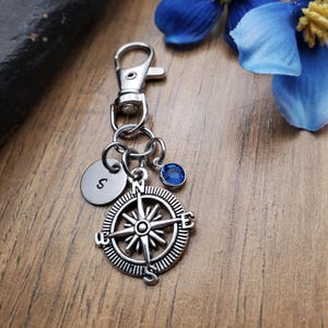 May include: Silver compass keychain with a blue gemstone and a silver charm with the letter 'S' engraved on it.