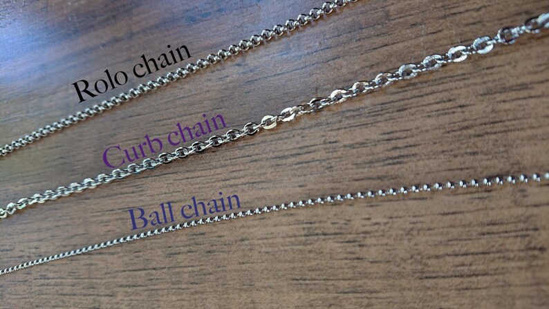 May include: Three different types of silver chains laid out on a wooden surface. The chains are labeled "Rolo chain", "Curb chain", and "Ball chain".