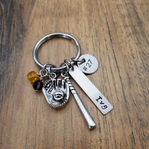 May include: A silver keychain with a baseball glove, bat, and beads. The keychain also has a silver tag that says "#27" and another tag that says "Ivy".