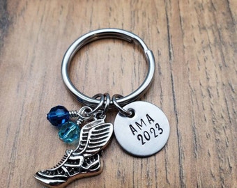 May include: Silver keychain with a winged shoe charm, two blue glass beads, and a round tag that says "AMA 2023".