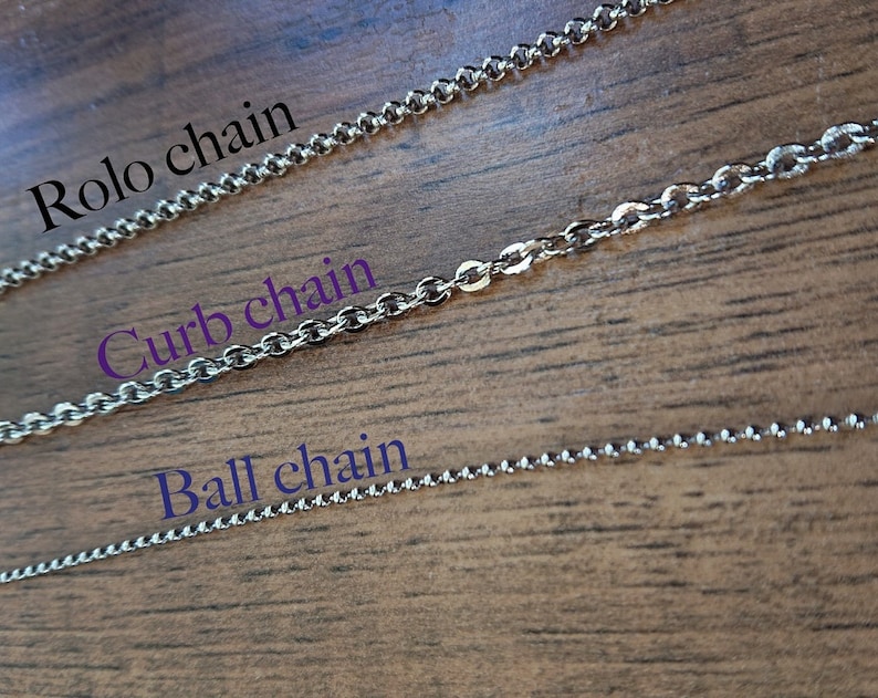 May include: Three different types of silver chains: rolo chain, curb chain, and ball chain. The chains are laid out on a wooden surface.