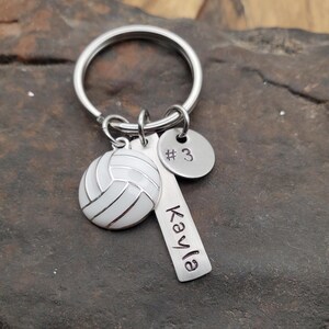 May include: Silver keychain with a white volleyball charm, a silver charm with the number 3, and a silver charm with the name "Kayla" engraved on it.