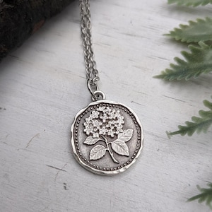 Peut inclure: Un collier pendentif argenté avec un motif floral détaillé. Le pendentif circulaire a une bordure en relief et une surface texturée. La chaîne en argent délicate complète le motif floral complexe du pendentif. Le pendentif mesure environ 2,5 cm de diamètre.