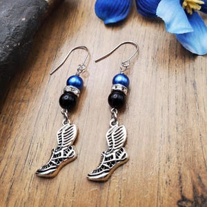 May include: A pair of silver earrings with blue and black beads and a winged shoe charm.