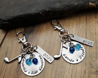 May include: Two silver keychains with music notes, blue beads, and personalized tags. One tag reads "Samantha Alto Saxophone 2025" and the other reads "Connie Piccolo 2025".