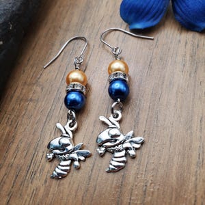 May include: A pair of silver bee earrings with blue and gold beads. The bee charms are detailed and have a 3D effect.