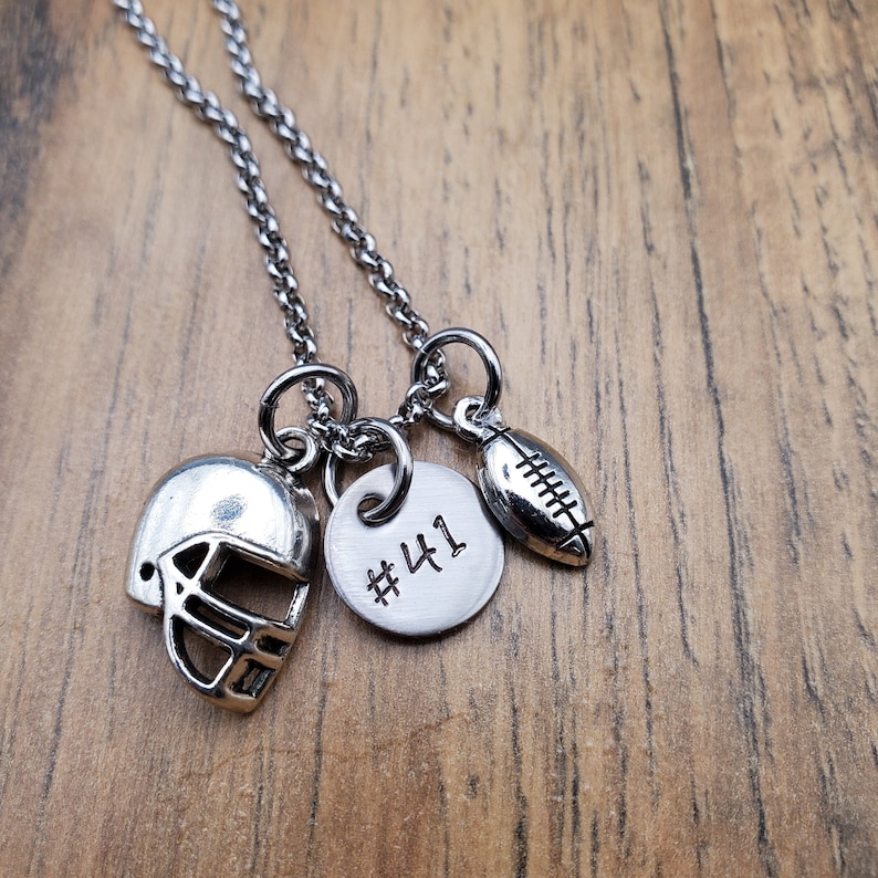 May include: A silver necklace with three charms: a football, a football helmet, and a round charm with the number "#41" engraved on it.