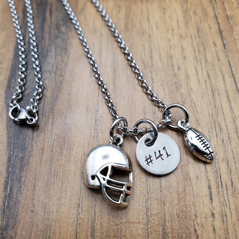 May include: A silver chain necklace with three charms: a football, a football helmet, and a round charm with the number "#41" engraved on it.