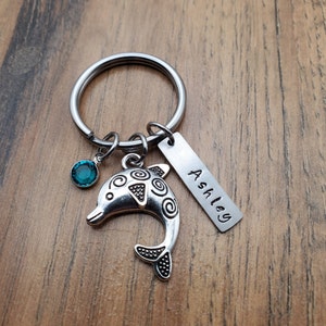 May include: Silver dolphin keychain with a teal blue gem and a personalized tag that reads "Ashley".