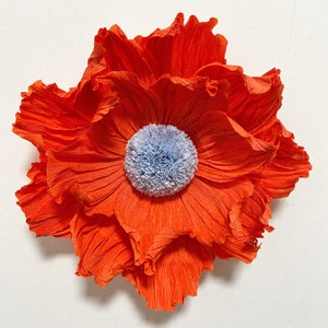 May include: A large, bright orange paper flower with a blue and white center. The flower is made of crinkled paper and has a delicate, layered texture.