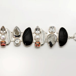 May include: A silver bracelet with a black agate, clear quartz, and a pearl. The bracelet has a toggle clasp and a chain link extension.