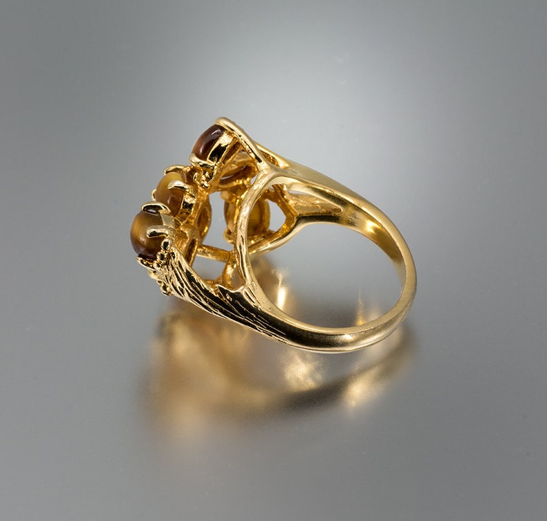 May include: Gold ring with a cluster of three brown tiger's eye stones set in a delicate, ornate design.