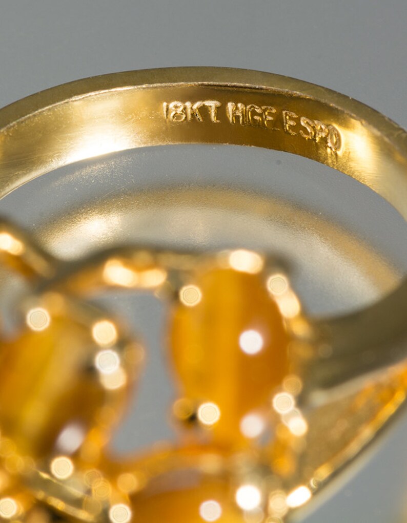 May include: Close-up of the inside of a gold ring with the inscription "18KT HGE ESPO".