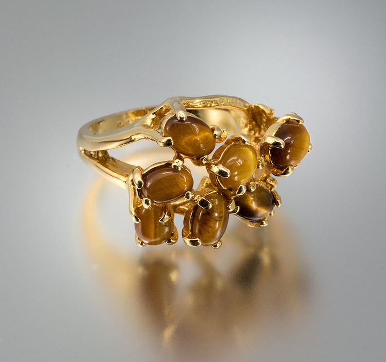 May include: A gold ring with a cluster of oval-shaped tiger's eye stones. The stones are set in a gold band and are arranged in a cascading pattern.