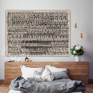 May include: A black and white sheet music print with musical notes and clefs on a beige background. The print is hanging on a wall above a bed with a gray duvet and white pillows.