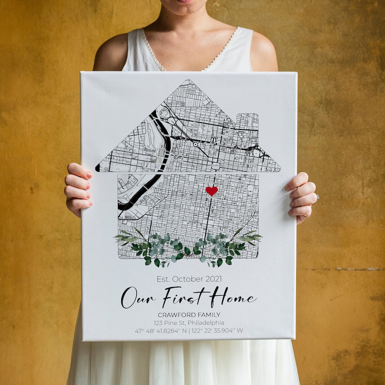 Puede incluir: Una impresi&oacute;n en lienzo blanco con un mapa de una ciudad en blanco y negro en forma de casa. El mapa tiene un coraz&oacute;n rojo en el centro. El texto "Est. octubre 2021 Nuestro primer hogar Crawford Family 123 Pine St, Filadelfia 47&deg; 48' 41.8284" N | 122&deg; 22' 35.904" W" est&aacute; impreso debajo del mapa.